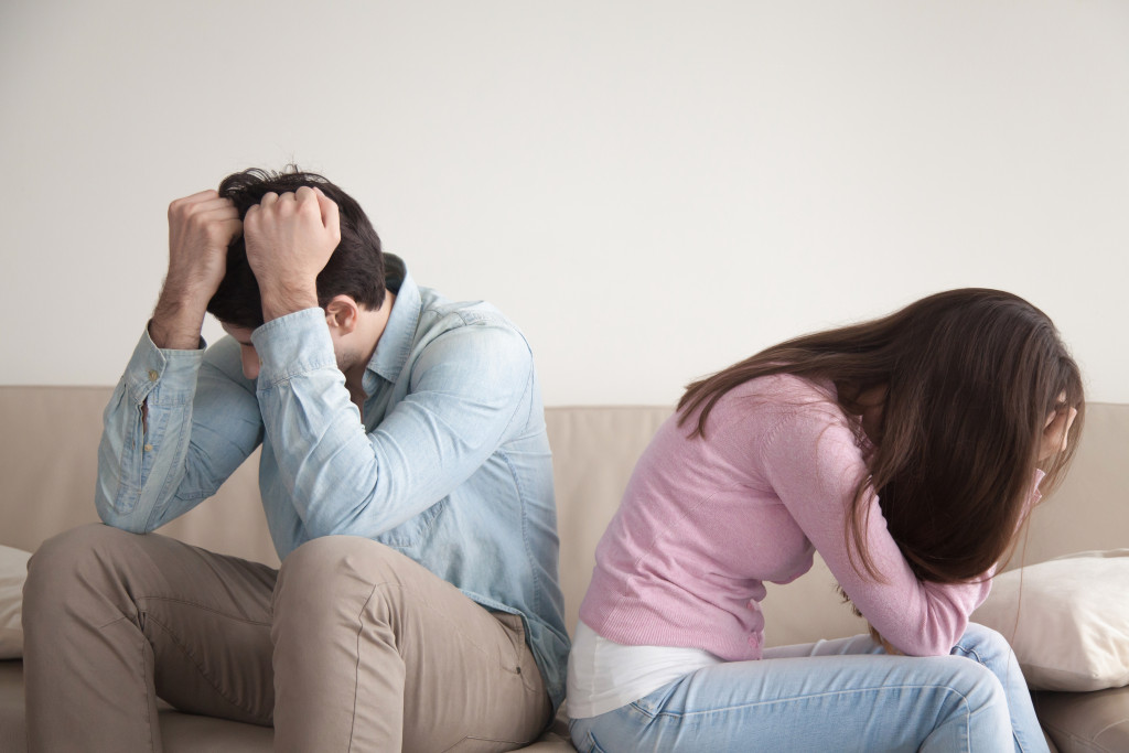 A couple holding their heads down with their backs towards each other on a couch