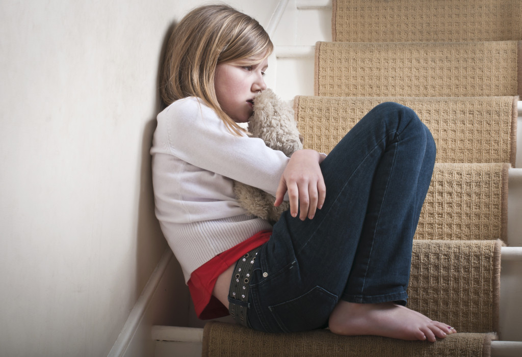 A sad young girl hugging a teddy bear on the stairs