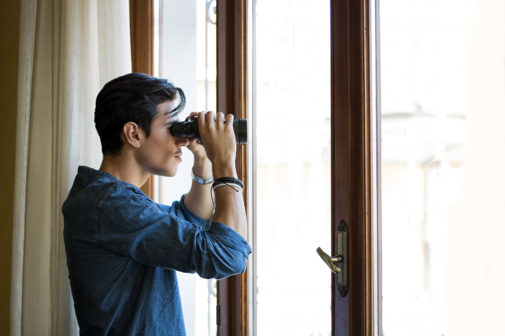 A man looking through a window with binoculars